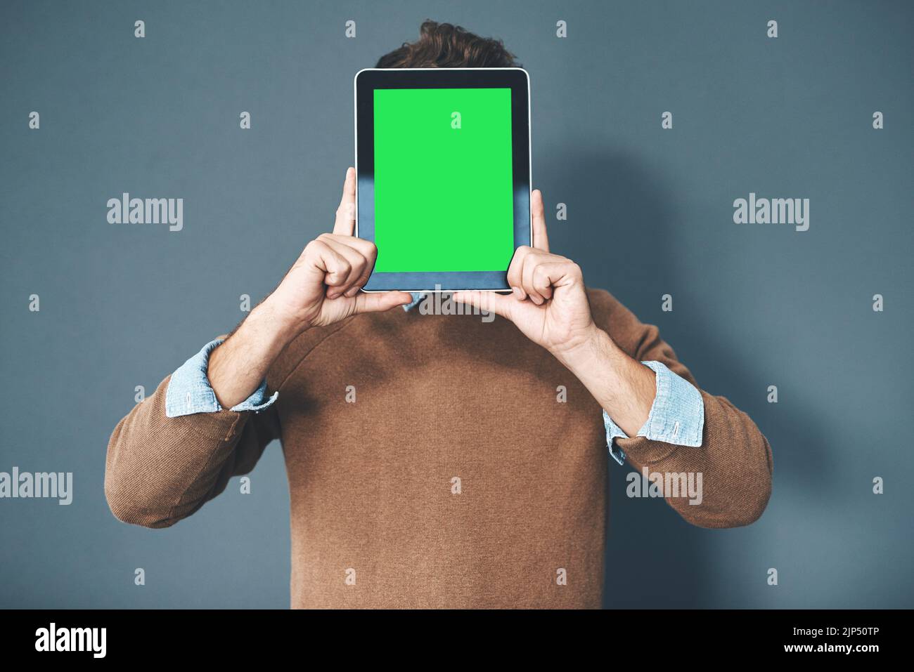 Tablet mit grünem Bildschirm, Chroma-Taste und Kopierraum, der von einem Mann vor grauem Hintergrund gehalten wird. Technologie und Werbung oder Marketing eines digitalen Unternehmens Stockfoto