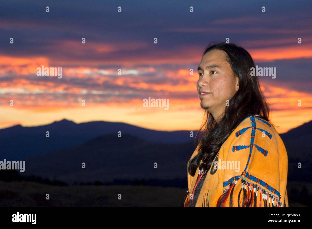 Der junge indianische Mann im traditionellen Hemd aus geperlter Hirschhaut denkt bei einem herrlichen Sonnenuntergang über den Northern Plains, Montana, über seine Zukunft nach Stockfoto