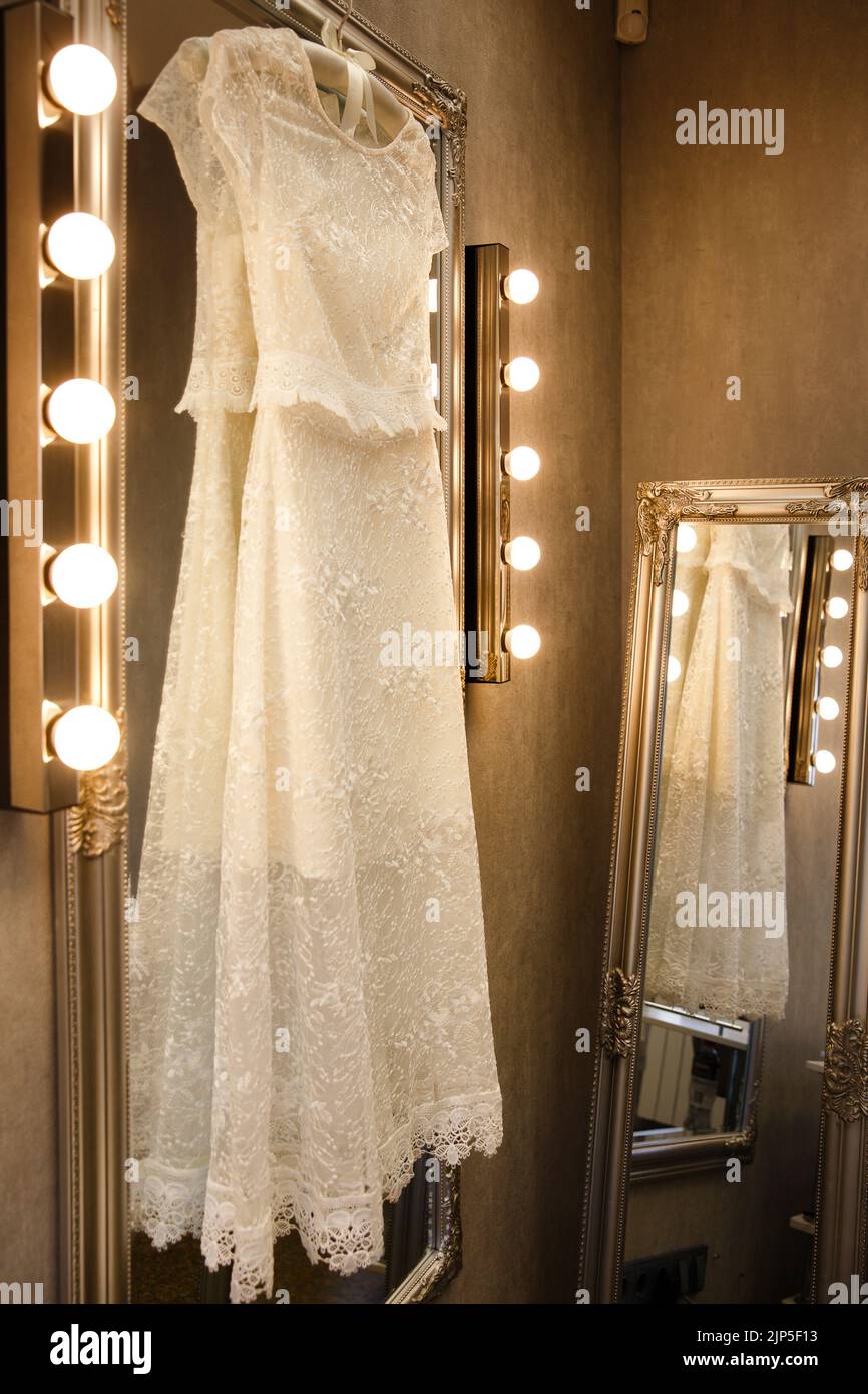 Hochzeitskleid, das auf einem Spiegel mit Lampen hängt. Stockfoto