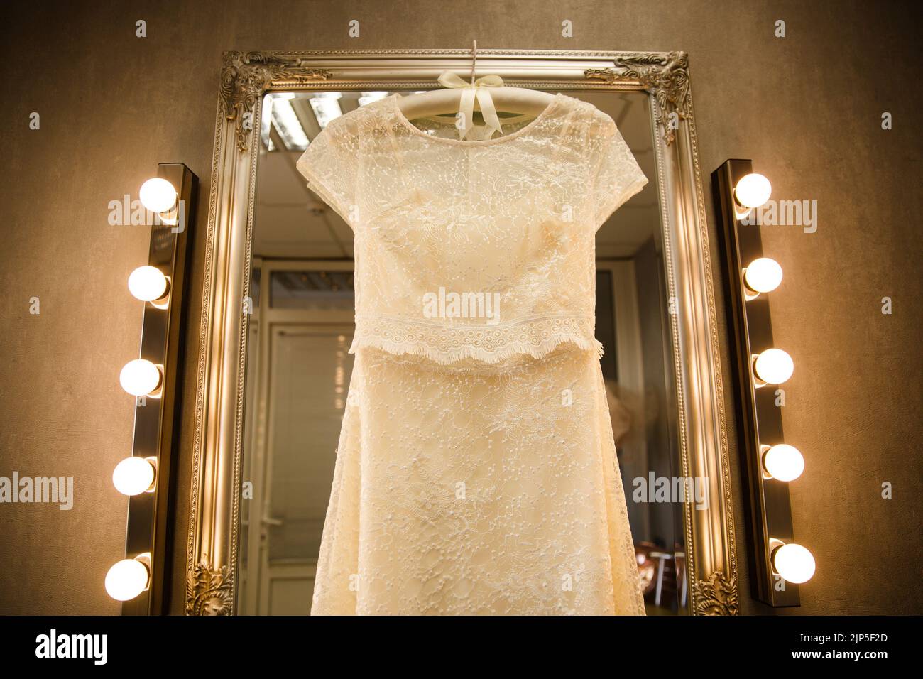 Hochzeitskleid, das auf einem Spiegel mit Lampen hängt. Stockfoto