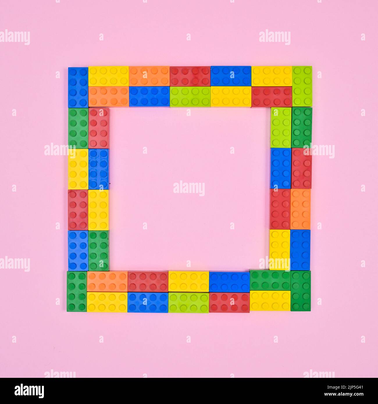 Bunte Ziegel Spielzeug auf pastellrosa Hintergrund. Ziegelrahmen. Flach liegend und mit viel Platz Stockfoto