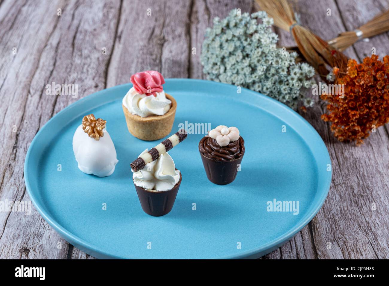 Raffiniertes Gebäck mit Schokoladenganache und Schlagsahne. Dehydrierte Blüten im Hintergrund. Stockfoto