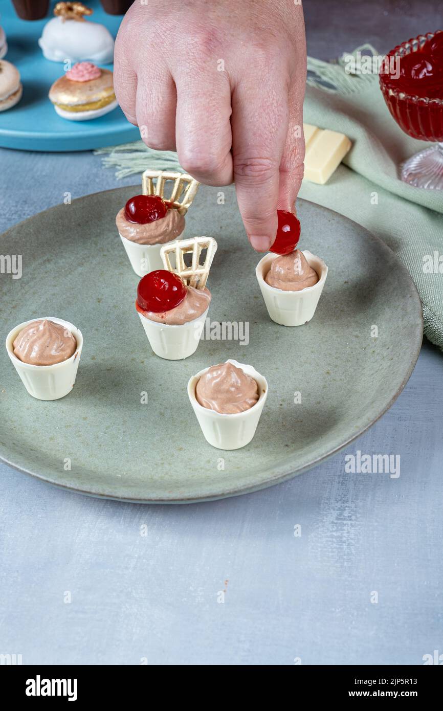 Konditorei mit Kirsche, kleine weiße Schokoladenbecher gefüllt mit Milchschokoladenmousse. Stockfoto