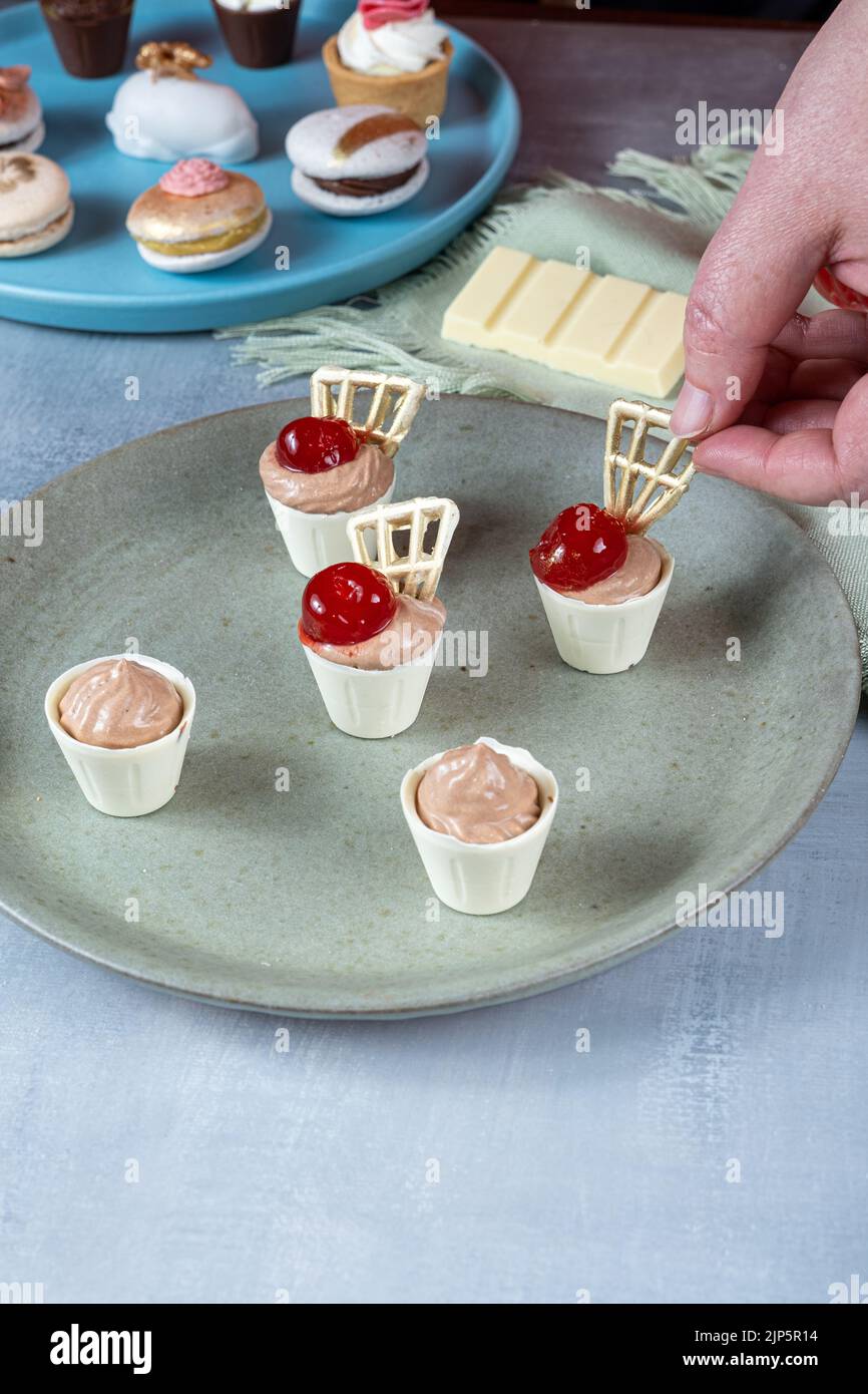 Konditor beendet weiße Schokoladenbecher, gefüllt mit Milchschokoladenmousse und Kirsche. Stockfoto