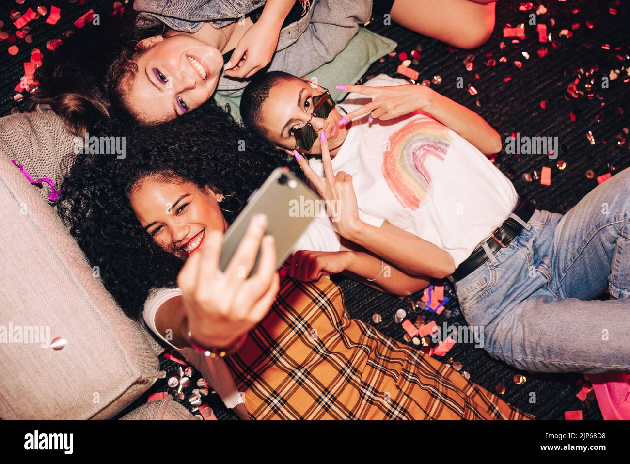 Nur süße Selfies. Blick aus der Perspektive von drei glücklichen Freunden, die ein Selfie machen, während sie auf dem Boden auf einer Hausparty liegen. Gruppe von fröhlichen Freundinnen Stockfoto