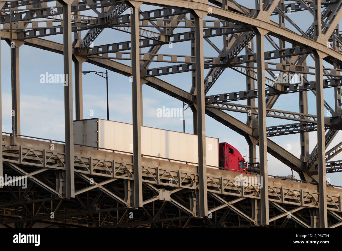 Ein roter Transporter mit weißem Anhänger fährt über eine Fachwerkbrücke. Stockfoto