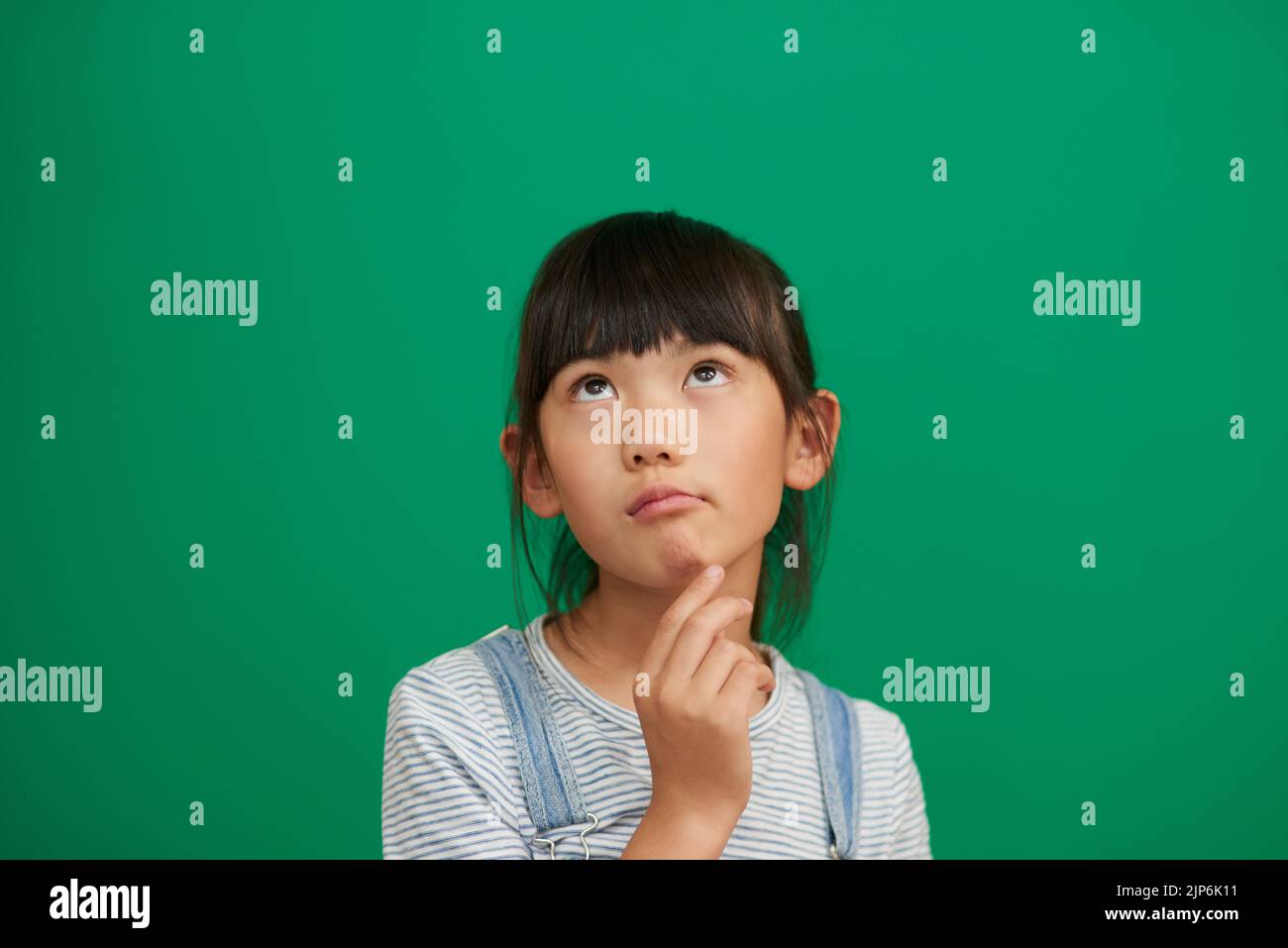 Was soll ich heute tun? Studioaufnahme eines entzückenden kleinen Mädchens, das vor grünem Hintergrund steht und nachdenkt. Stockfoto