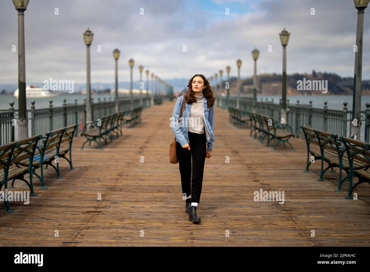 Unbeposed Portrait of Young Woman on Pier 7 Walking towards Camera with San Francisco Bay in the Background Stockfoto
