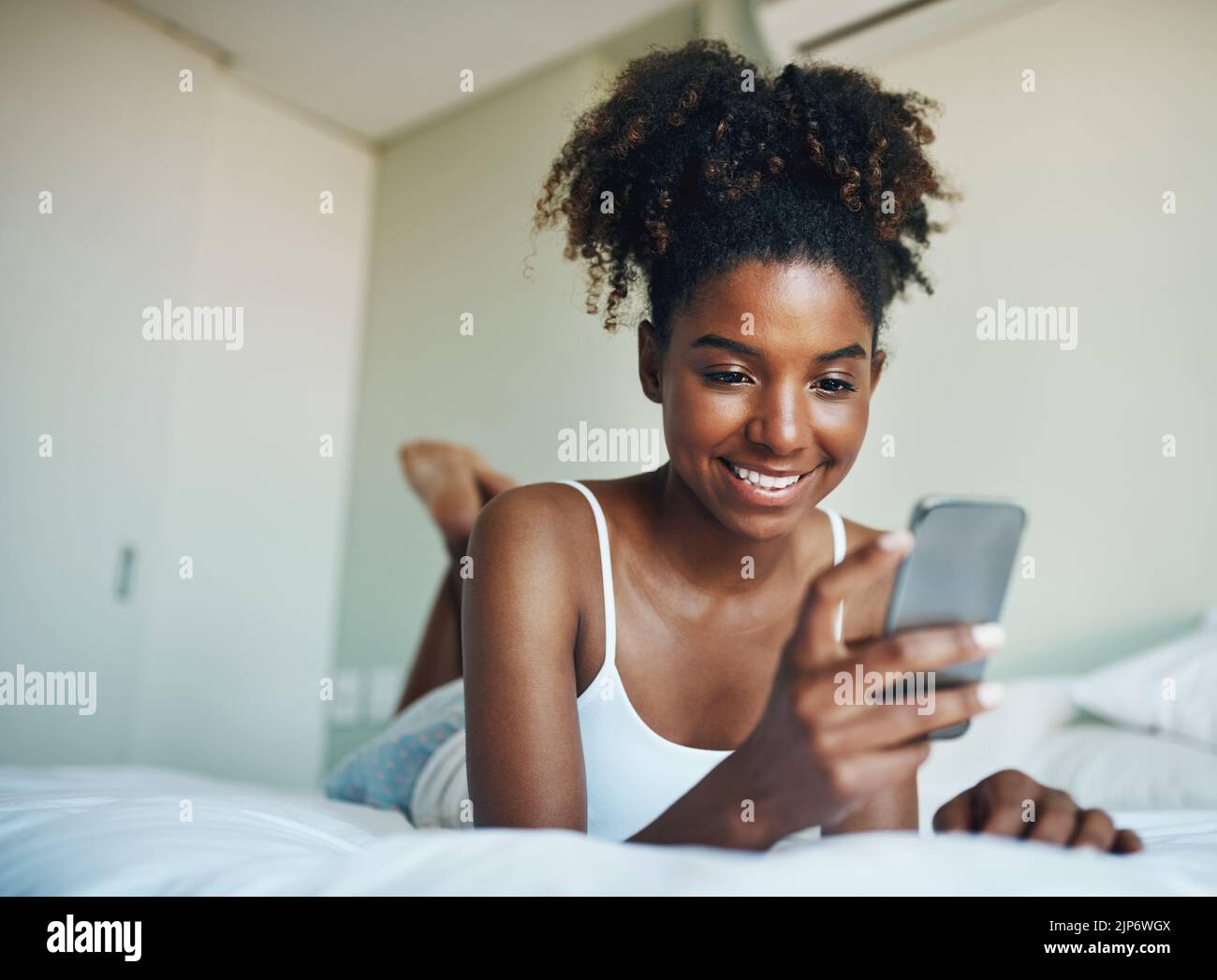 Ich überprüfe immer zuerst am Morgen meine sozialen Medien. Eine junge, schöne Frau benutzt ein Handy in ihrem Schlafzimmer zu Hause. Stockfoto