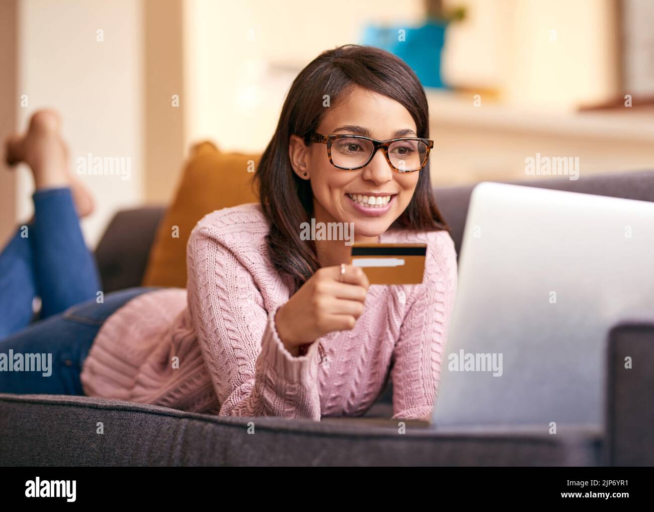 Eine attraktive junge Frau mit Laptop und Kreditkarte auf dem Sofa zu Hause. Stockfoto