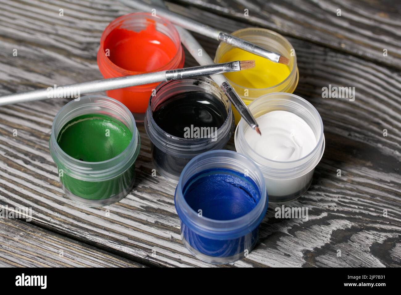 Ein Set aus Gouache und Bürsten. Farbdosen öffnen. Auf Kiefernbrettern. Nahaufnahme. Stockfoto