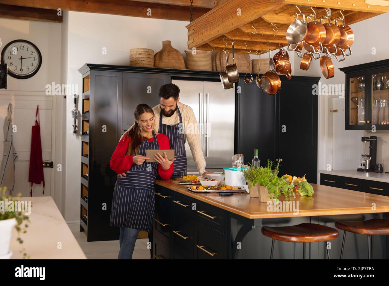 Glückliches kaukasisches Paar, das in der Küche Essen zubereitet, das Rezept umarmt und auf einem Tablet anschaut Stockfoto