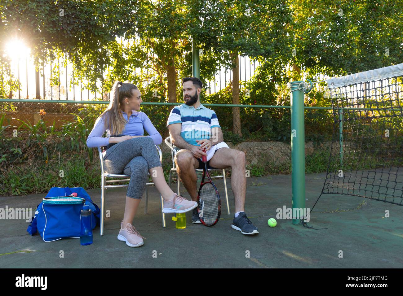 Kaukasisches Paar, das Tennis spielt und auf Stühlen sitzt und an der Seite eines Tennisplatzes im Freien spricht Stockfoto