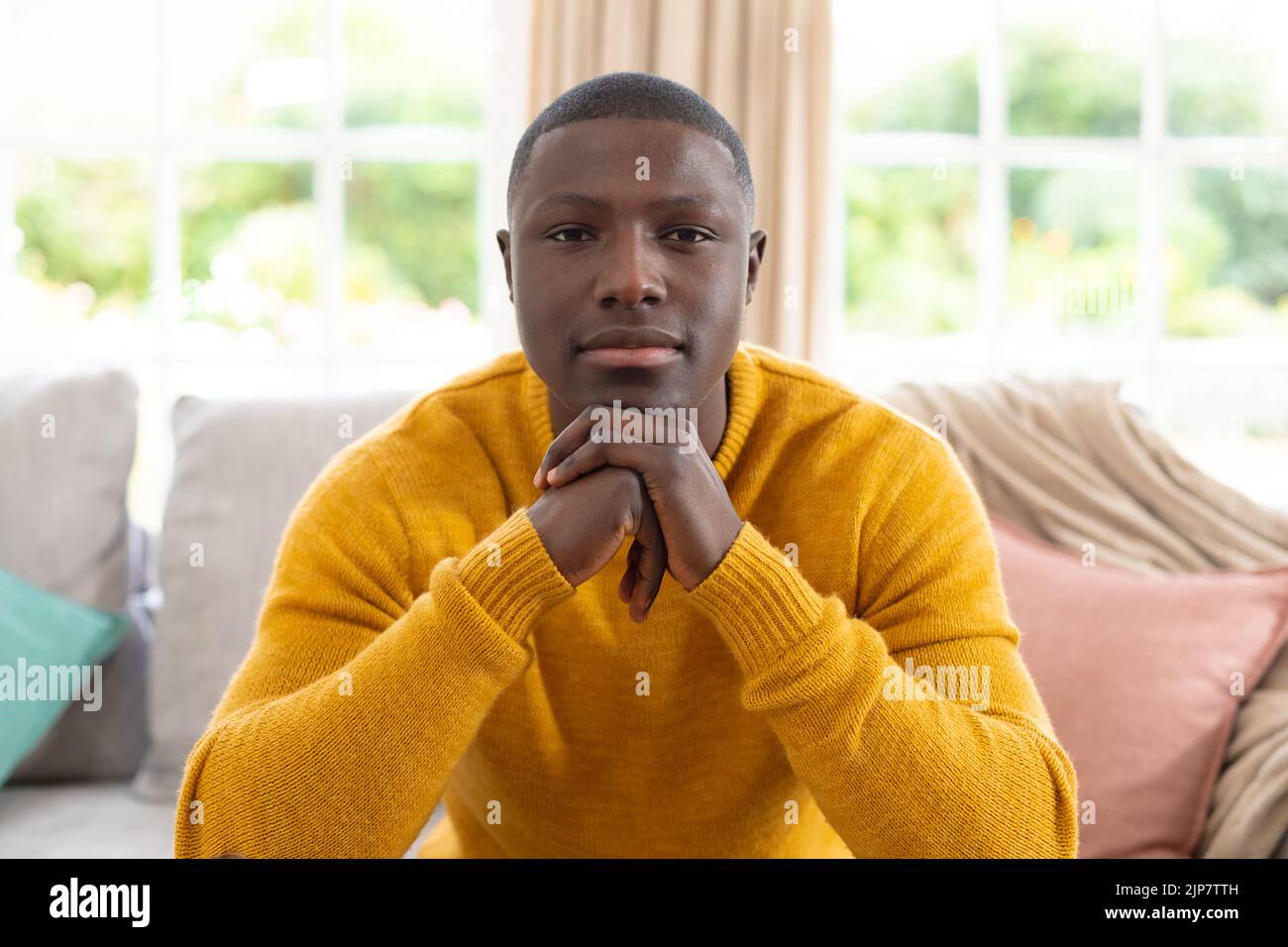 Porträt eines lächelnden afroamerikanischen Mannes zu Hause, der auf der Couch sitzt und direkt zur Kamera schaut Stockfoto