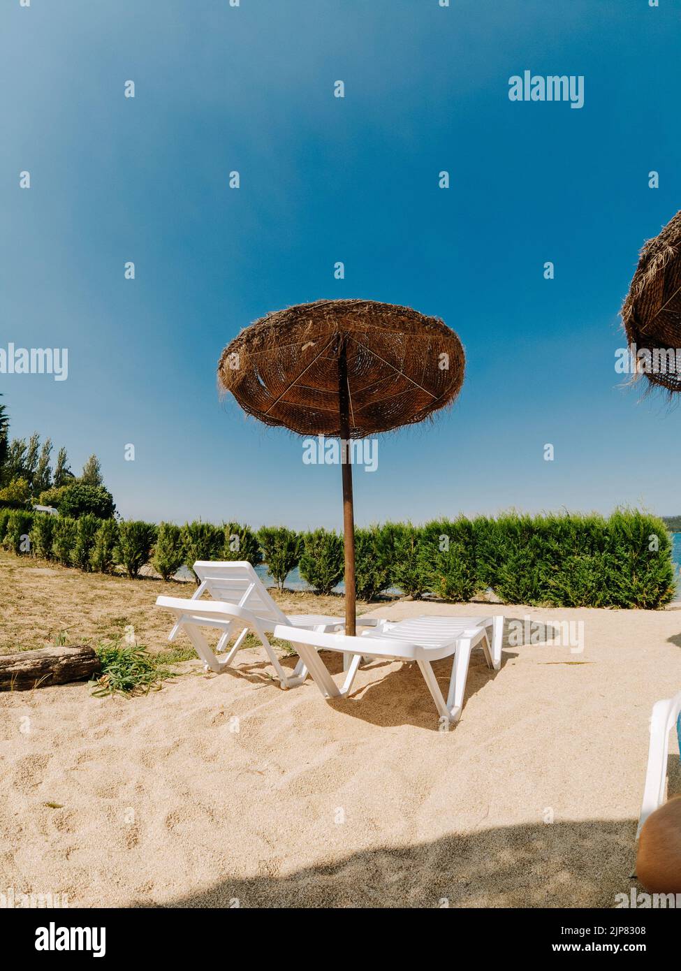 Ein paar Liegestühle mit einem Strohschirm in der Nähe des Flusses Stockfoto