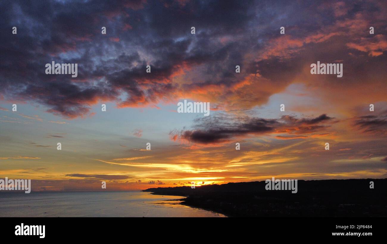 Schöner, goldener, orangefarbener Sonnenuntergang, der sich auf der Oberfläche des wellenförmigen Ozeans am Sommerabend an der Küste der Stadt Bayawan spiegelte. Stockfoto