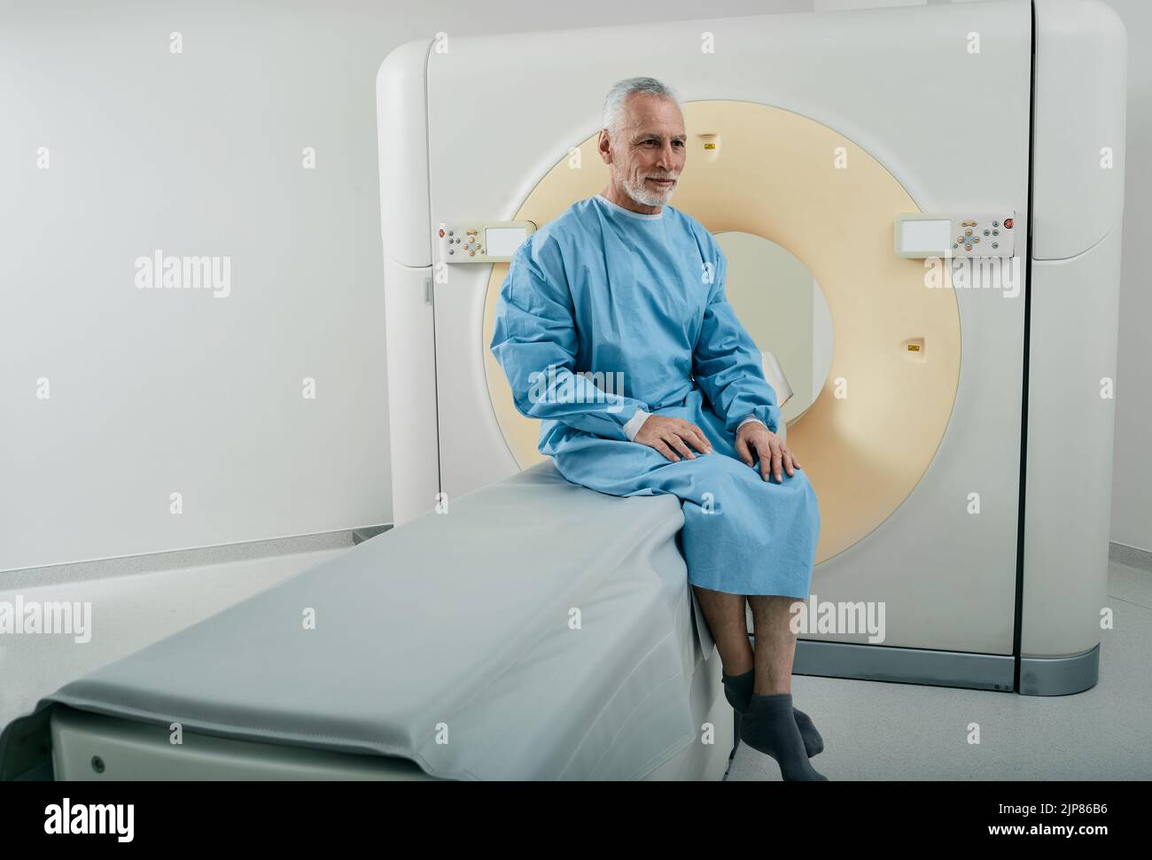 Alter Mann mit CT-Scan-Verfahren sitzt auf CT-Maschinenscanner in der Radiologie Abteilung des Krankenhauses Stockfoto