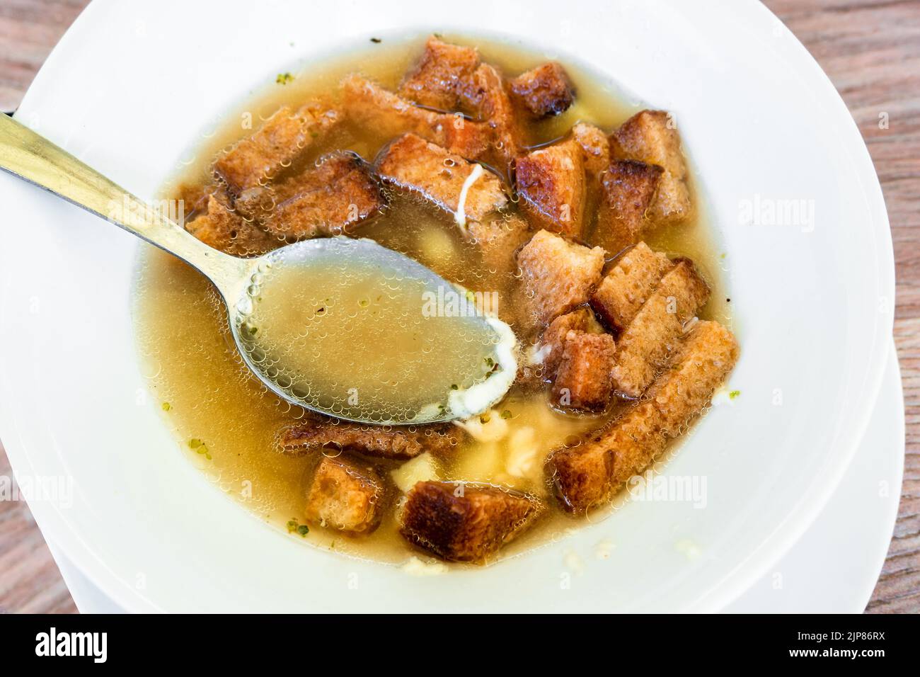 Knoblauchsuppe mit in Scheiben geröstetem Brot und Käse und Löffel auf weißem Teller, Nahaufnahme. Traditionelle tschechische Küche. Stockfoto