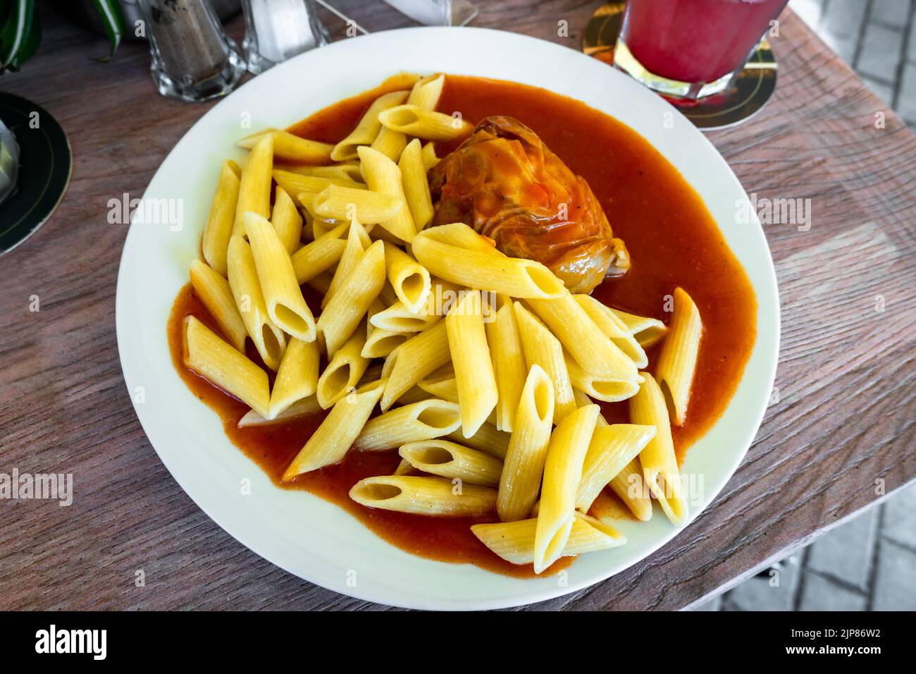 Penne und gebackene gefüllte gelbe Paprika mit Fleisch in würziger Tomatensauce auf weißem Teller auf Tisch mit Limonade, Nahaufnahme. Stockfoto