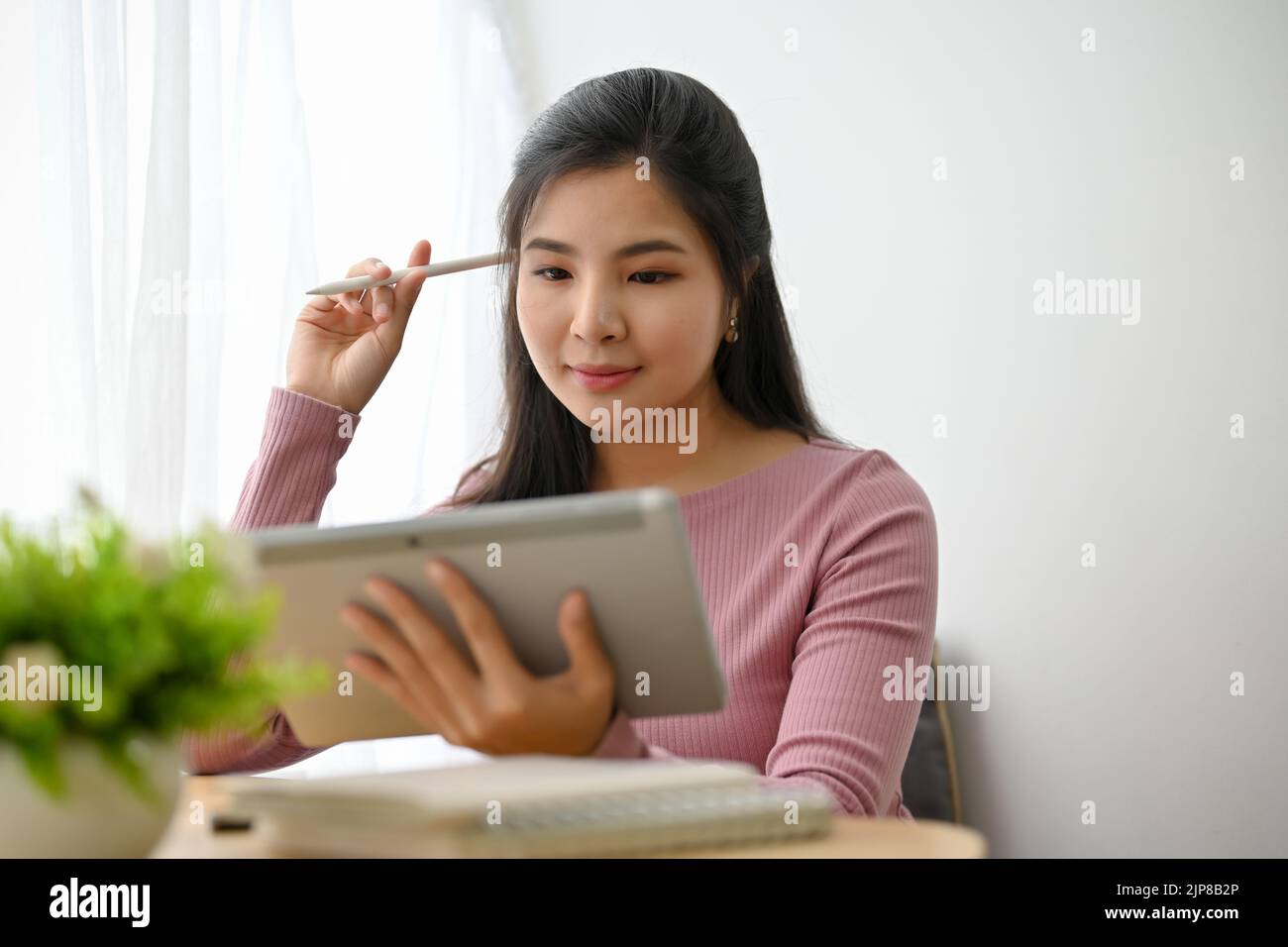 Schöne junge asiatische weibliche College-Studentin arbeitet mit einem digitalen Tablet-Touchpad an ihren Online-Hausaufgaben. Stockfoto