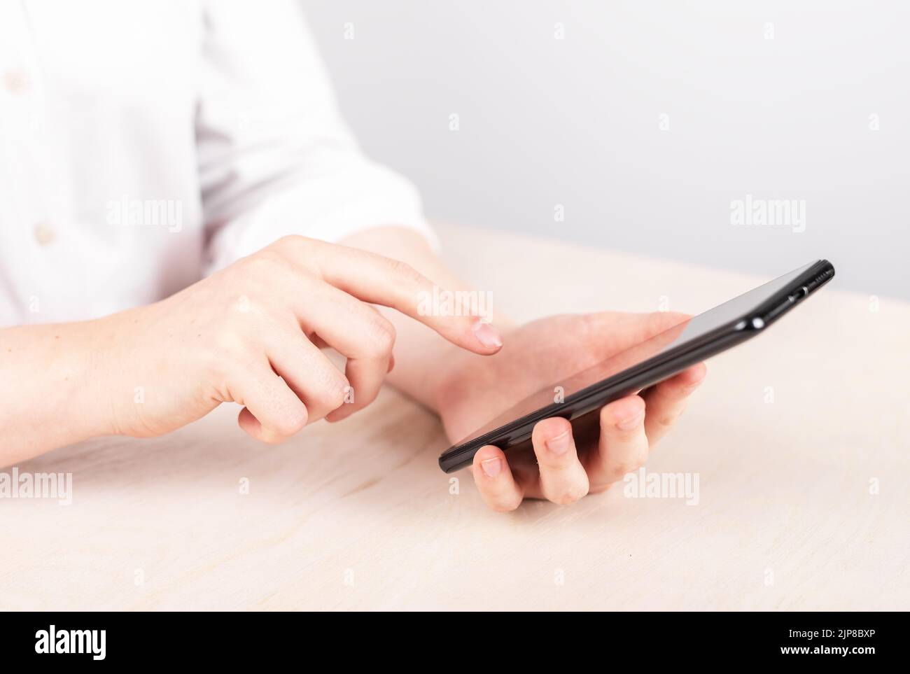 Frau Zeigefinger auf OK-Taste am Telefon. Frau, die am Tisch sitzt und das Smartphone hält, um über soziale Medien im Internet zu surfen. Hoher pH-Wert Stockfoto