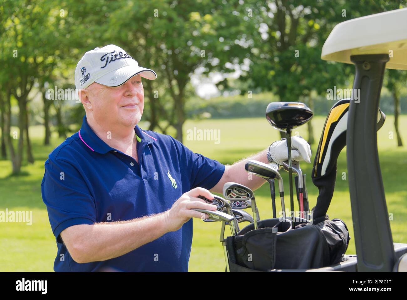 Eine flache Aufnahme eines alten Mannes, der eine Baseballmütze trägt und Golfschläger aus einer Golftasche auswählt Stockfoto