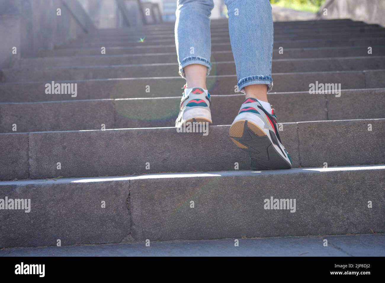 Die Beine der Frau in Jeans und Sneakers gehen eine steile Treppe hoch Stockfoto