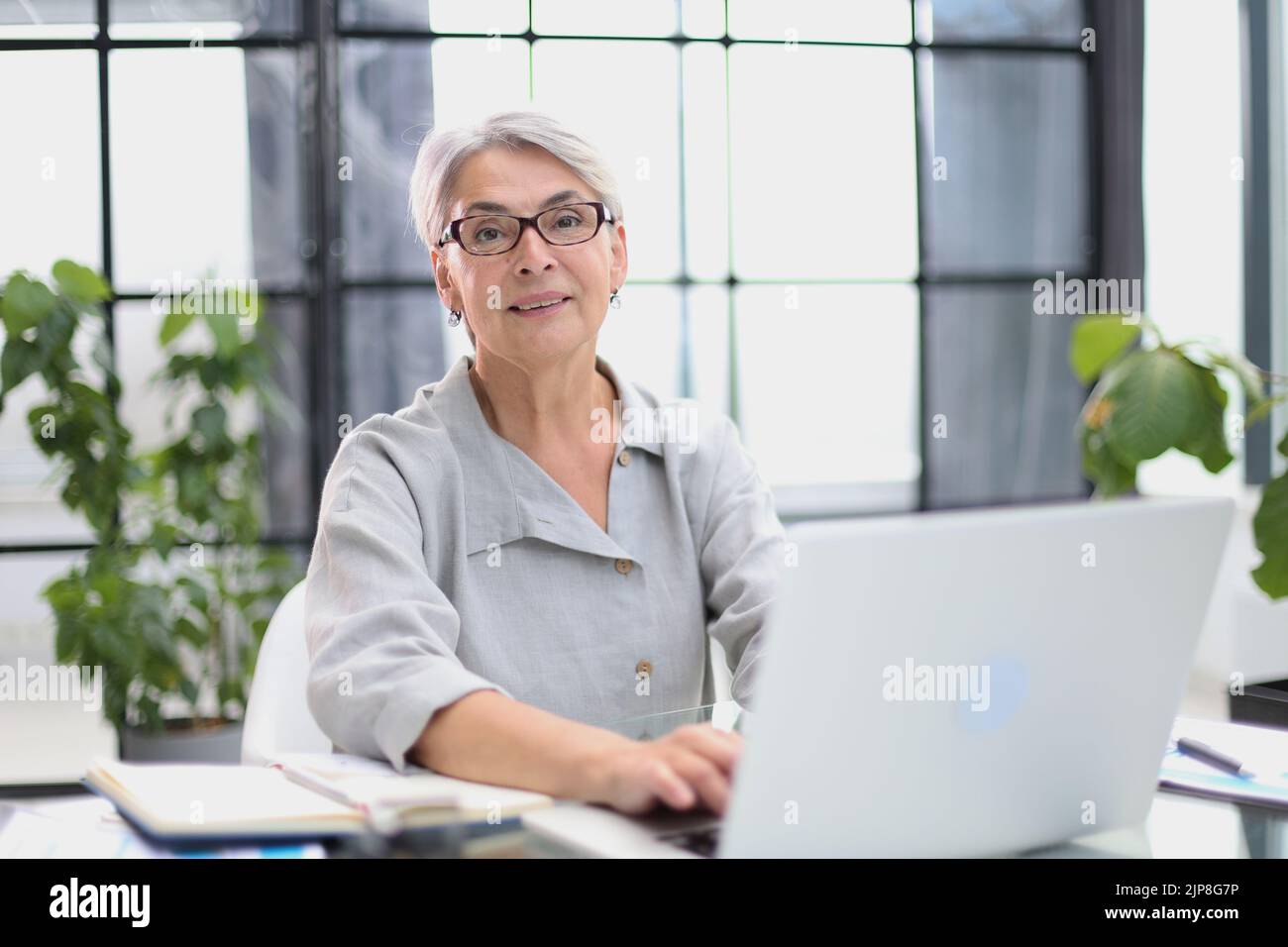 Lächelnde 60-jährige Geschäftsfrau, die einen Computer benutzt Stockfoto