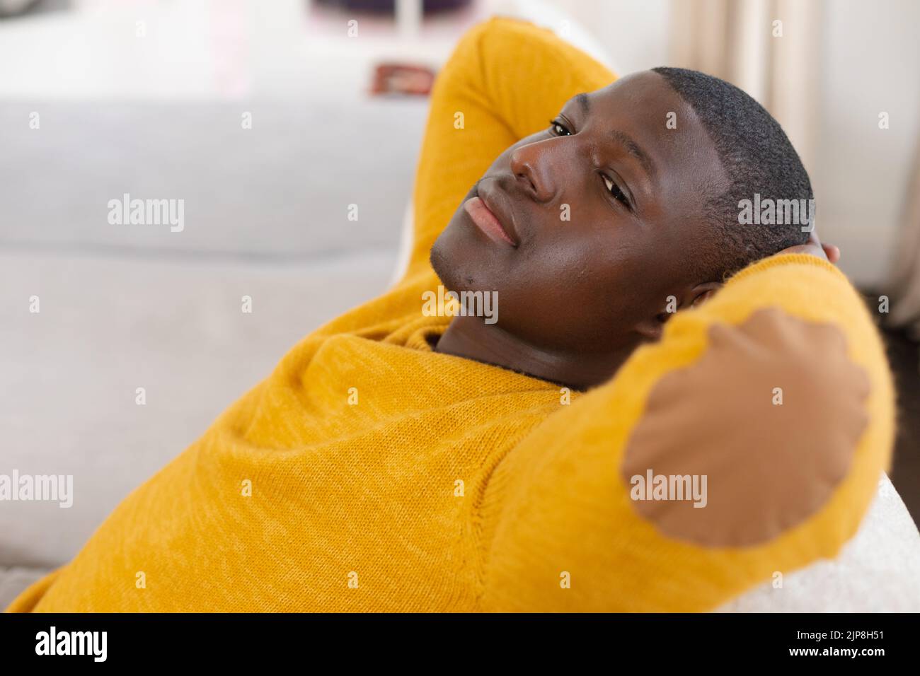 afroamerikanischer Mann zu Hause, der mit den Armen hinter dem Kopf auf der Couch zurückliegt und wegschaut Stockfoto