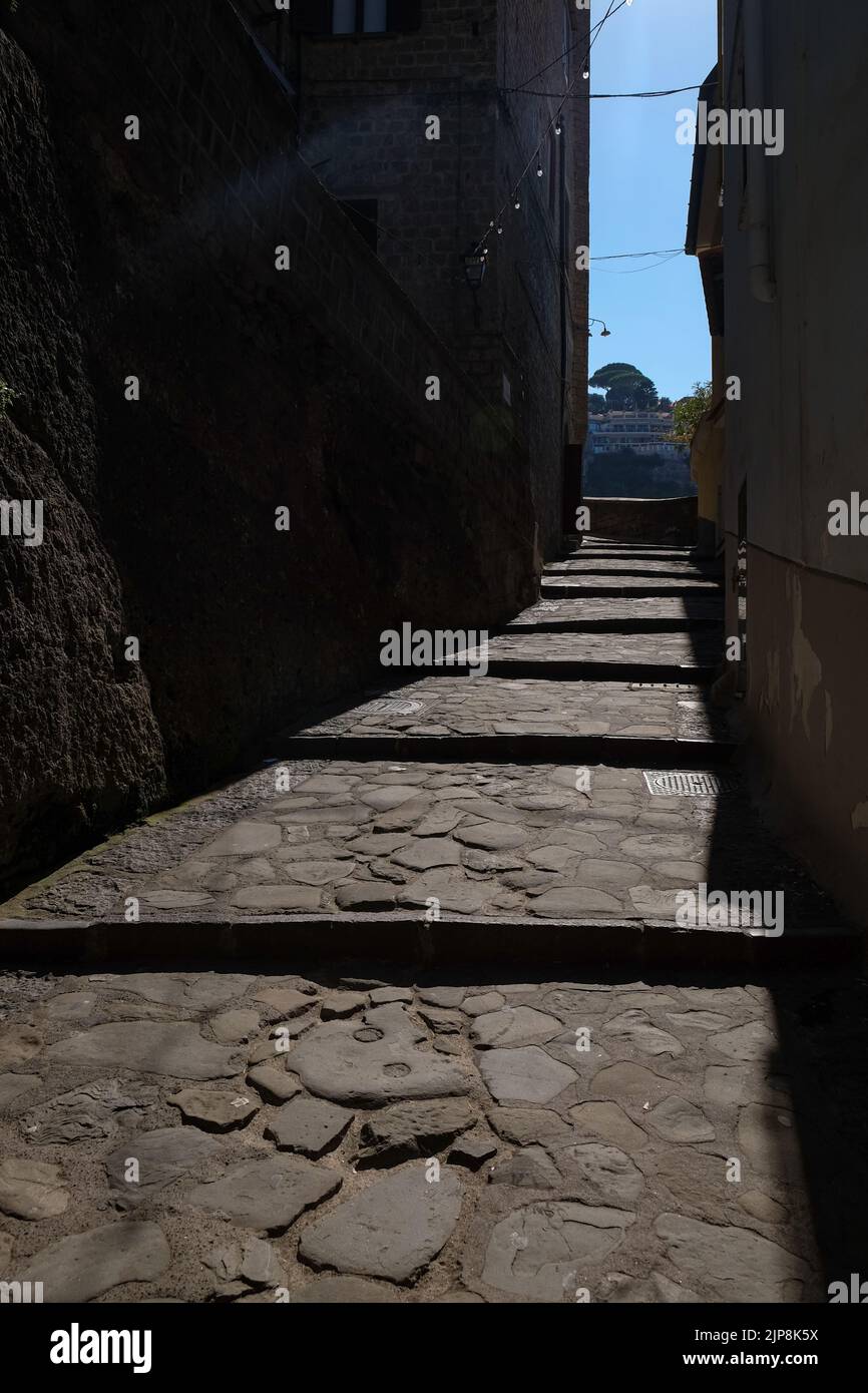 Die enge, stufenförmig gepflasterte, leere Straße von Sorrento in der Nähe der Marina Grande hat eine stimmungsvolle Aufnahme mit Sonneneinstrahlung auf die Straße und Schatten in den umliegenden Gebäuden. Stockfoto
