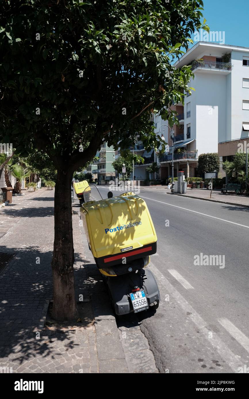Das Motorrad Poste Italiane parkt unter einem Baum unter der Mittagssonne, damit der Sitz und der Lenker nicht zu heiß werden. Stockfoto