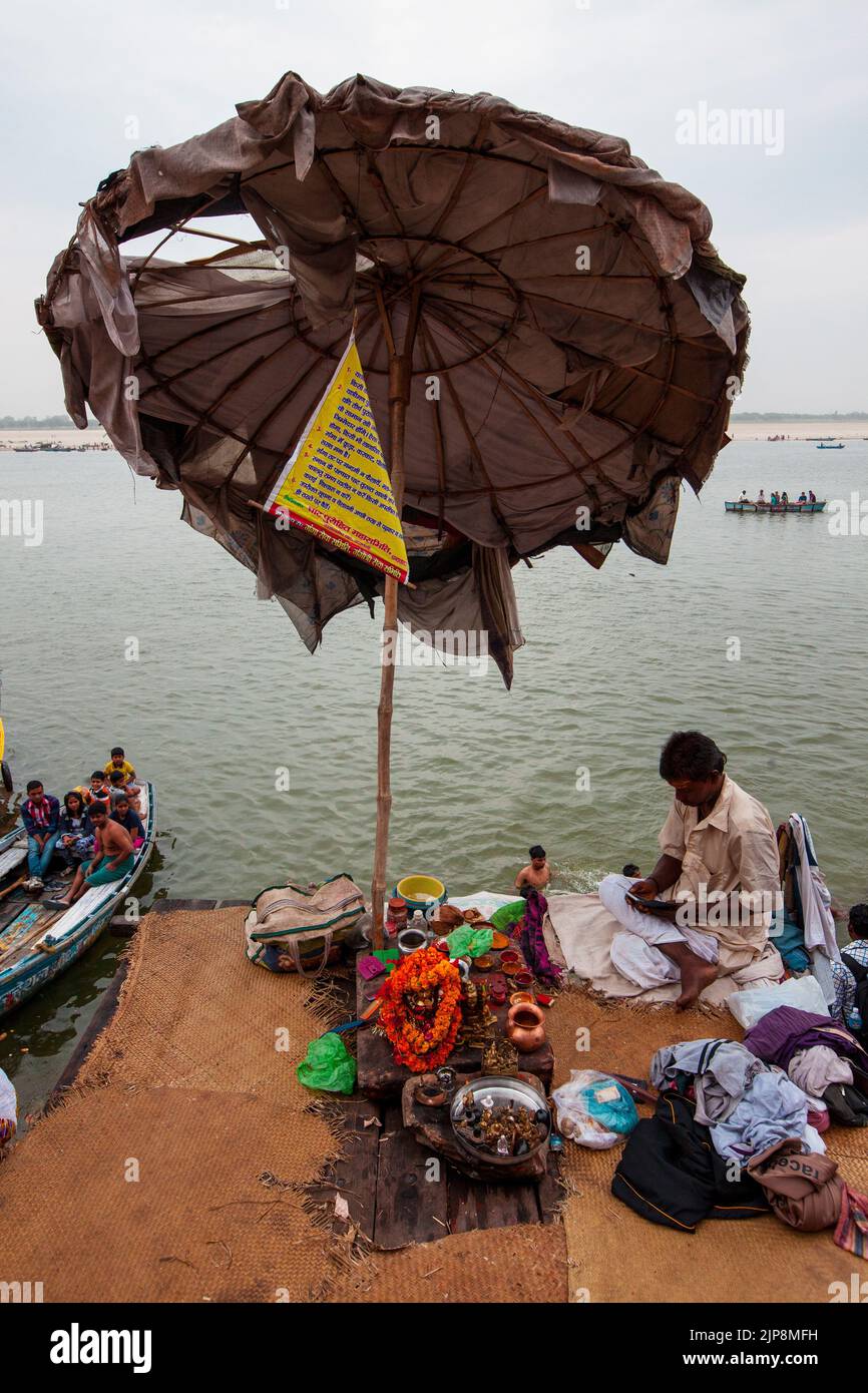 Priester, der unter einem riesigen Regenschirm bei Dashashwamedh Ghat am Ganga-Fluss Ganges sitzt, Varanasi, Banaras, Benaras, Kashi, Uttar Pradesh, Indien Stockfoto