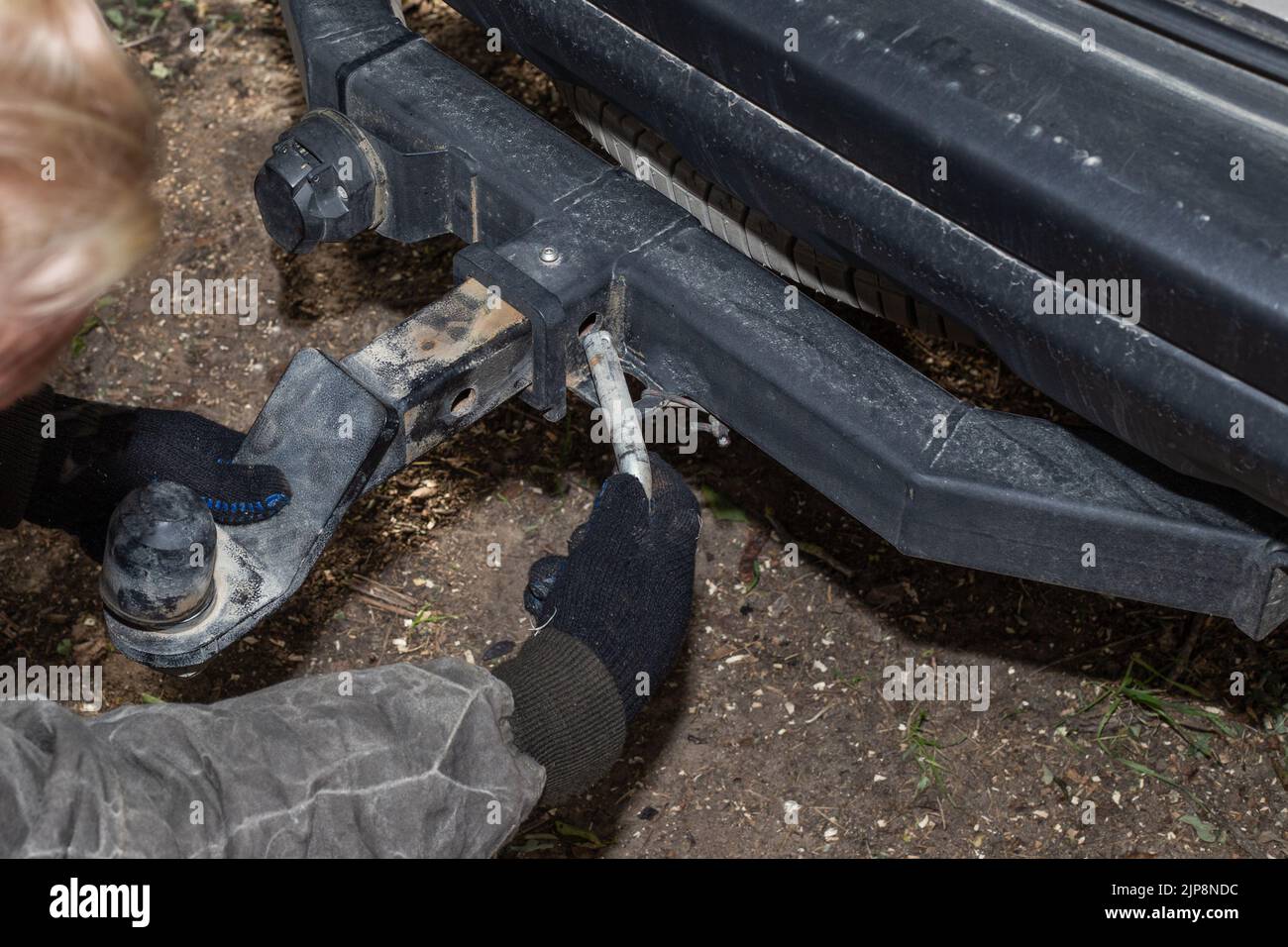 Ein Mann montiert eine eiserne Schleppstange auf einem Auto, um einen Anhänger zu schleppen. Gerät für den Transport. Stockfoto