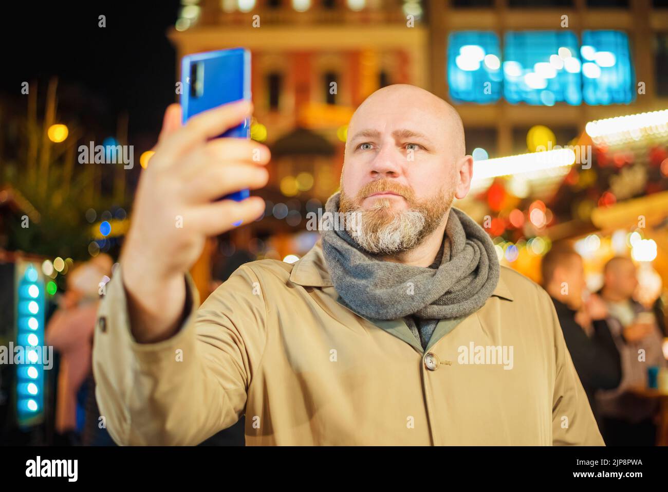 Ein Erwachsener fotografiert mit seinem Smartphone auf einem Weihnachtsmarkt in der Stadt. Der Mann nimmt Selfie mit dem Smartphone auf Stockfoto