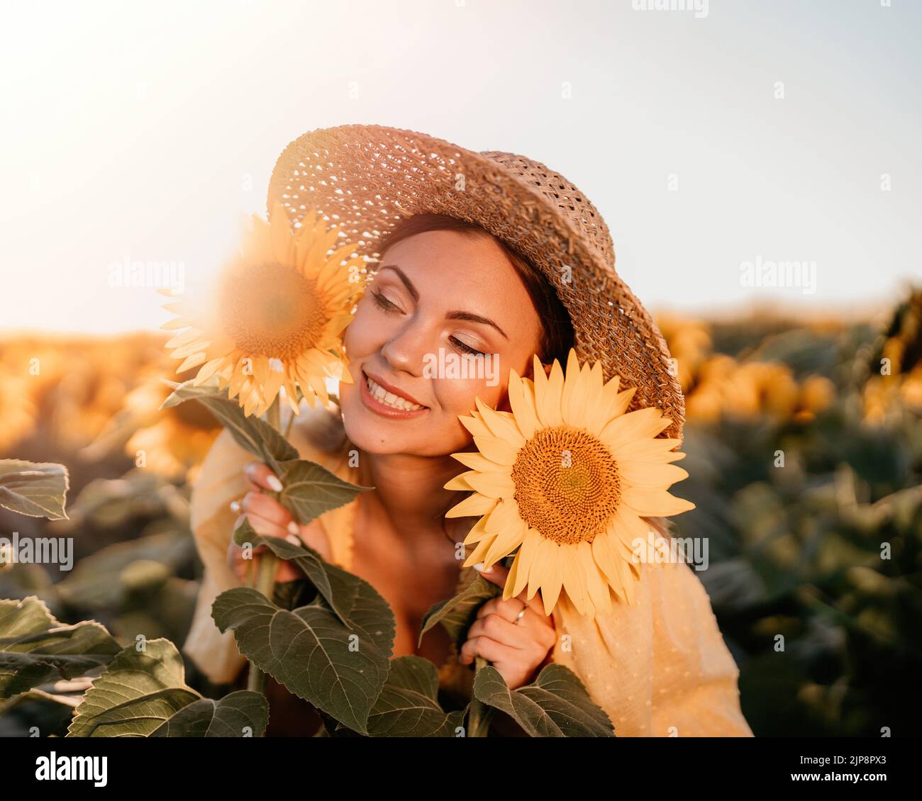 Schöne junge Frau in Strohhut posiert mit Sonnenblumen. Blühendes Feld. Glücklich lächelndes Mädchen. Trendiges Outfit im Vintage-Retro-Stil Stockfoto