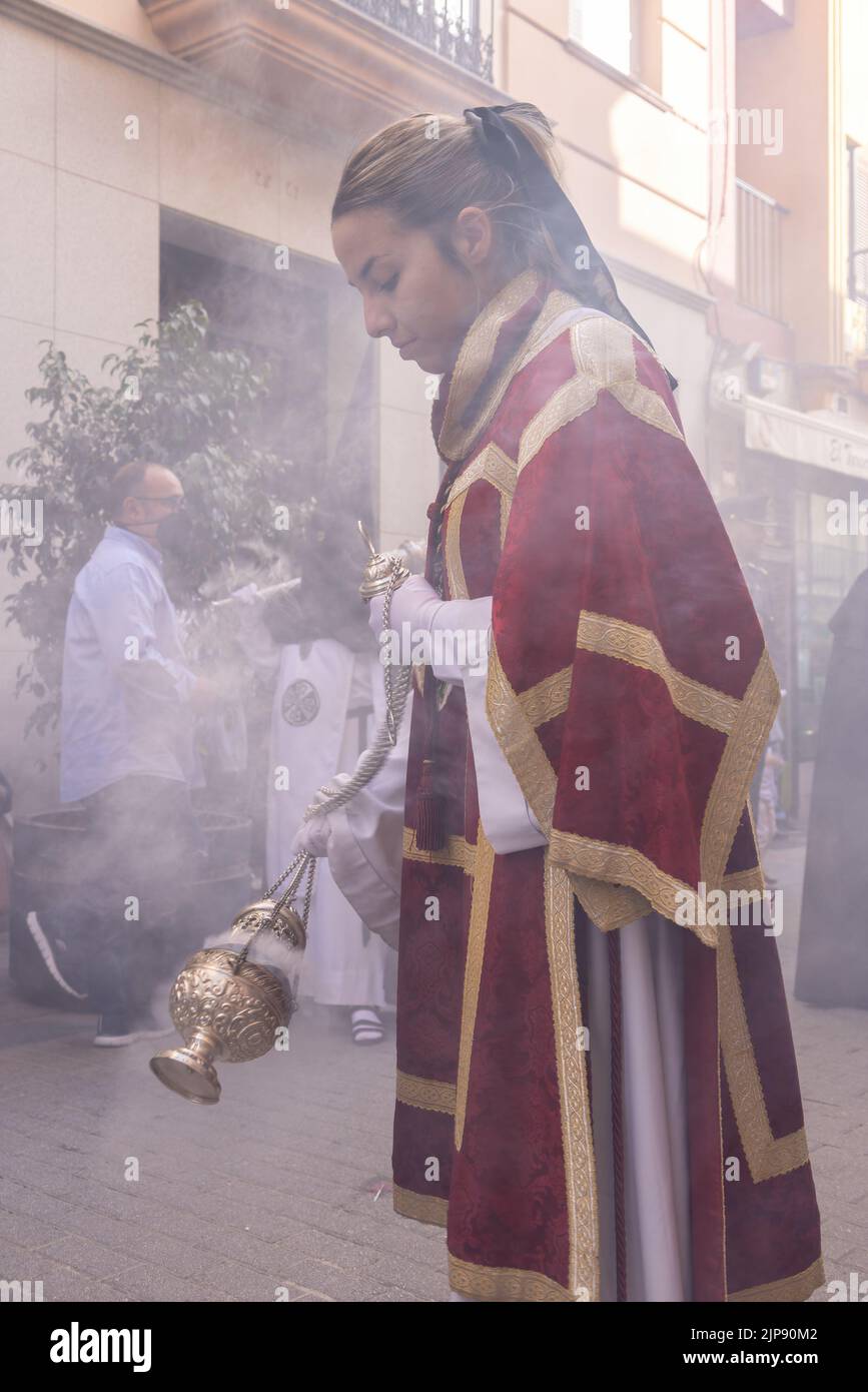 Huelva, Spanien - 10. April 2022: Weibliche Altarjunge oder Akolyte in der Prozession der Heiligen Woche schüttelte ein Räuchergefäß, um Rauch und Duft von Weihrauch zu erzeugen Stockfoto