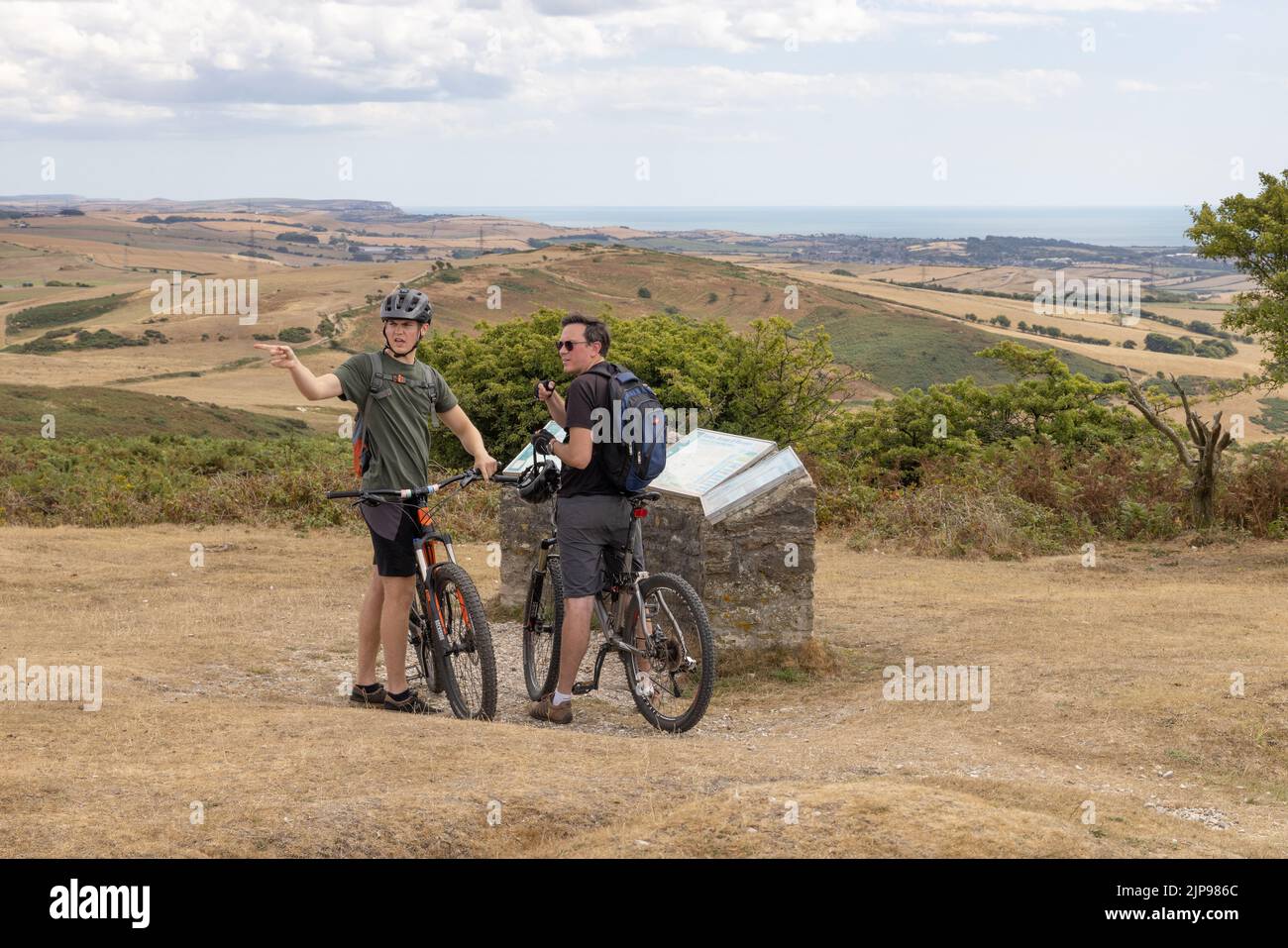 Radfahren auf dem Land in Großbritannien; zwei Männer im Alter von 30s Jahren mit ihren Fahrrädern auf dem Black Down Summit in , Dorset UK. Beispiel für Freizeitaktivitäten im Freien Stockfoto