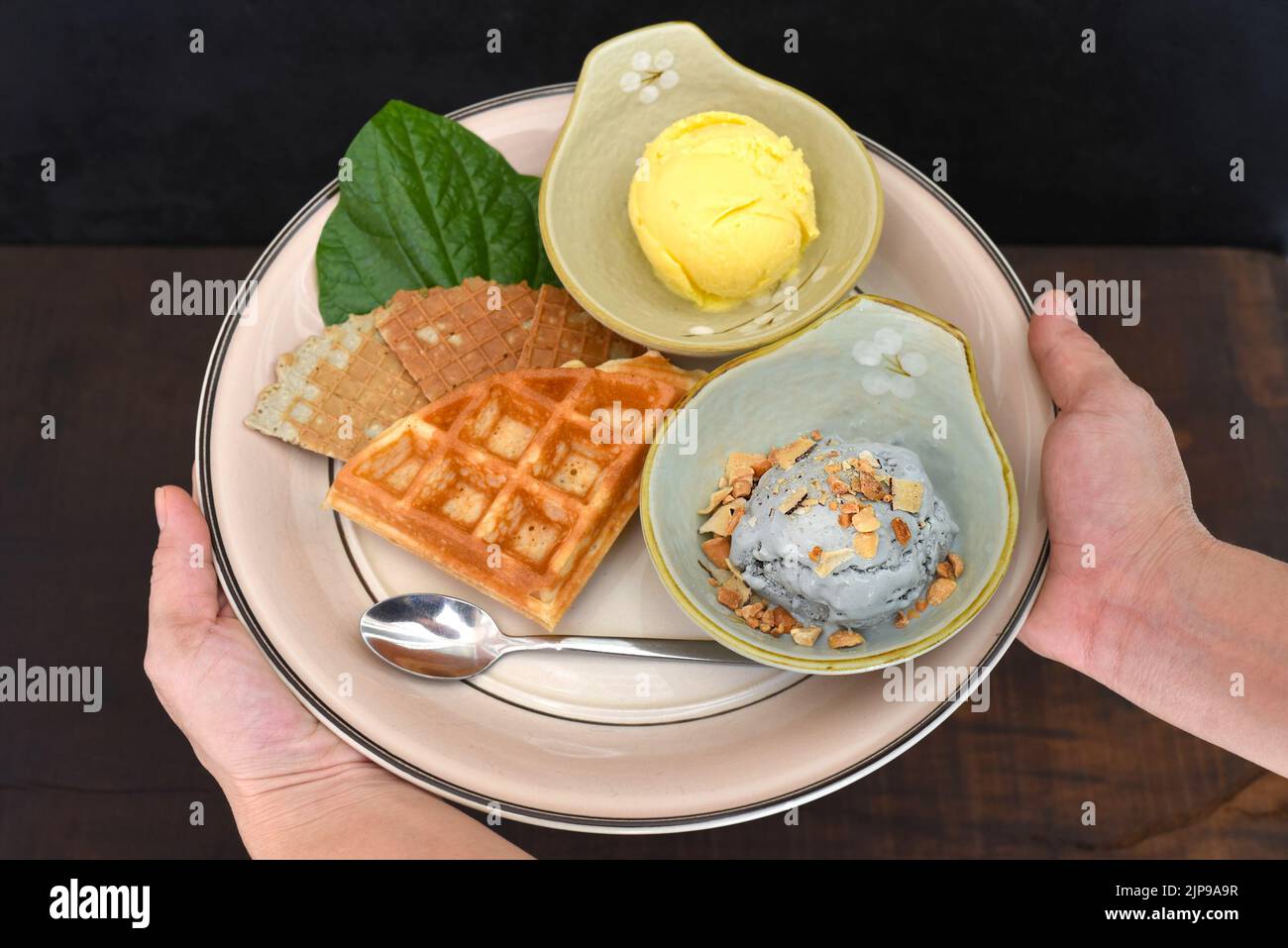 Hände halten Gericht mit Bio-Eis und belgischen Waffeln auf schwarzem Hintergrund Stockfoto