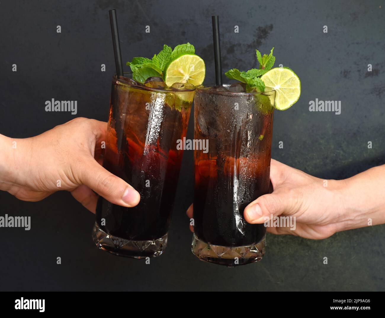 Hände klirrende Gläser mit Maulbeerwein Cocktails auf schwarzem Hintergrund Stockfoto