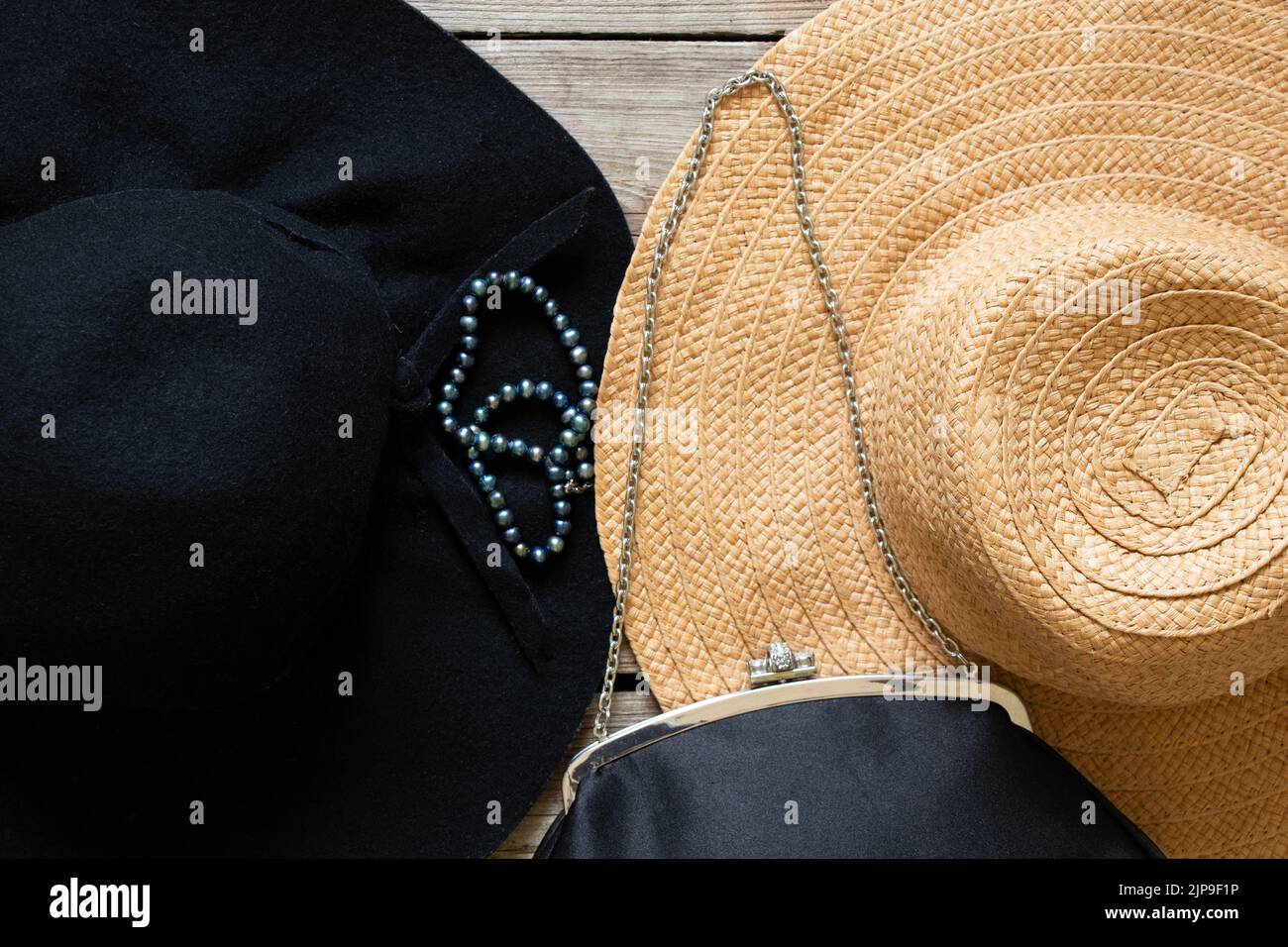 Schwarzer Frauenhut und schwarze Abendtasche sowie ein paar Perlen und ein Strohhut auf einem Holztisch, Mode und Trend Stockfoto