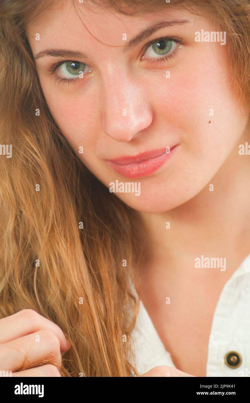 Eine junge Frau berührt ihre Haare, lächelt und schaut auf die Kamera. Stockfoto