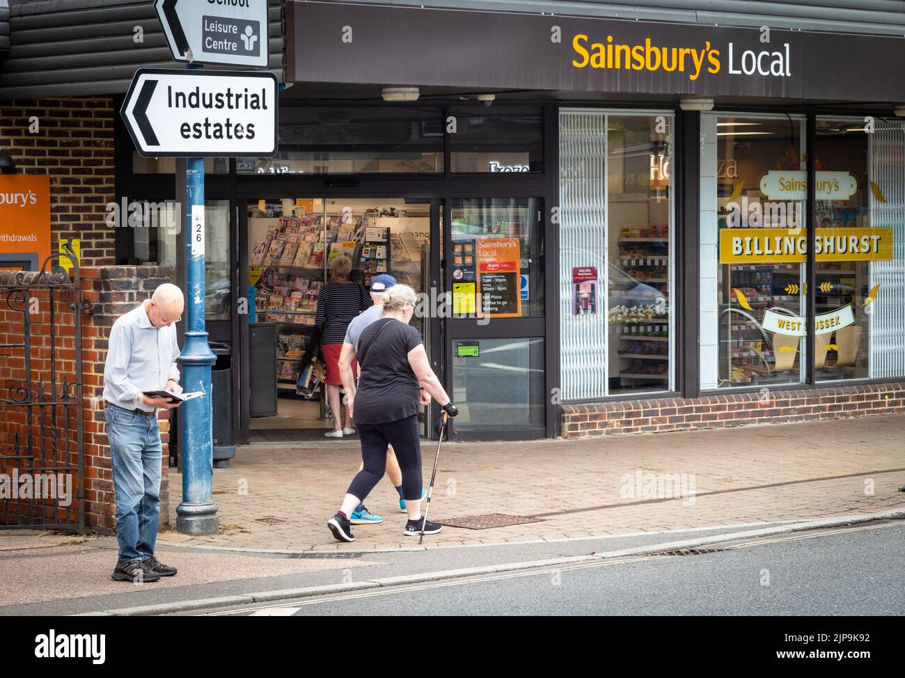 Billingshurst, West Sussex, Großbritannien, 16. August 2022. Eine Frau, die mit einem Gehstock und mit Mobilitätsprobleme unterwegs ist, geht an einem Sainsbury's Supermarkt in Billingshurst, West Sussex, Großbritannien, vorbei. In einem Bericht, der heute vom britischen Superstore veröffentlicht wurde, wurde festgestellt, dass Sainsbury's der am meisten beklagte Supermarkt in Großbritannien für behinderte Käufer ist. Stockfoto