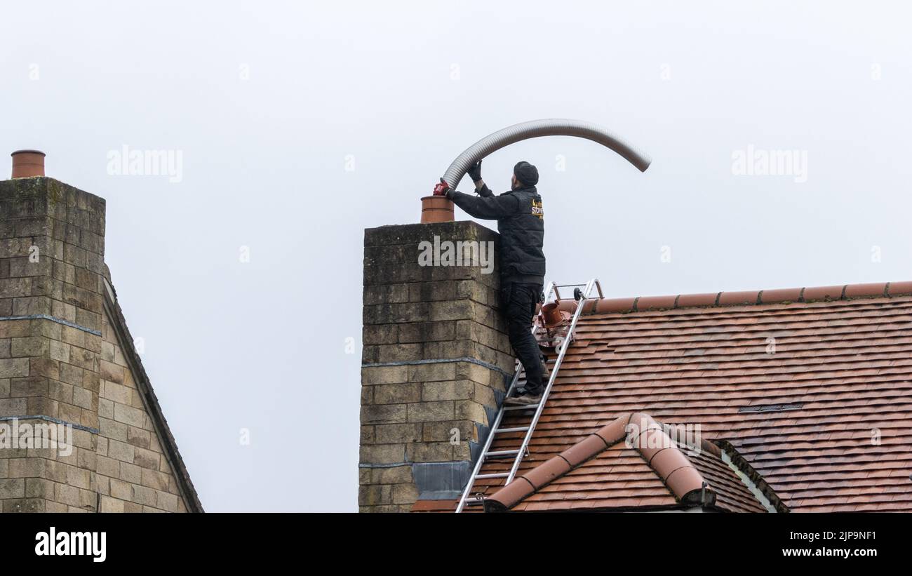Installation eines flexiblen Stahlrauchabgasklappes in einen Kamin während einer Holzofeninstallation, Großbritannien Stockfoto