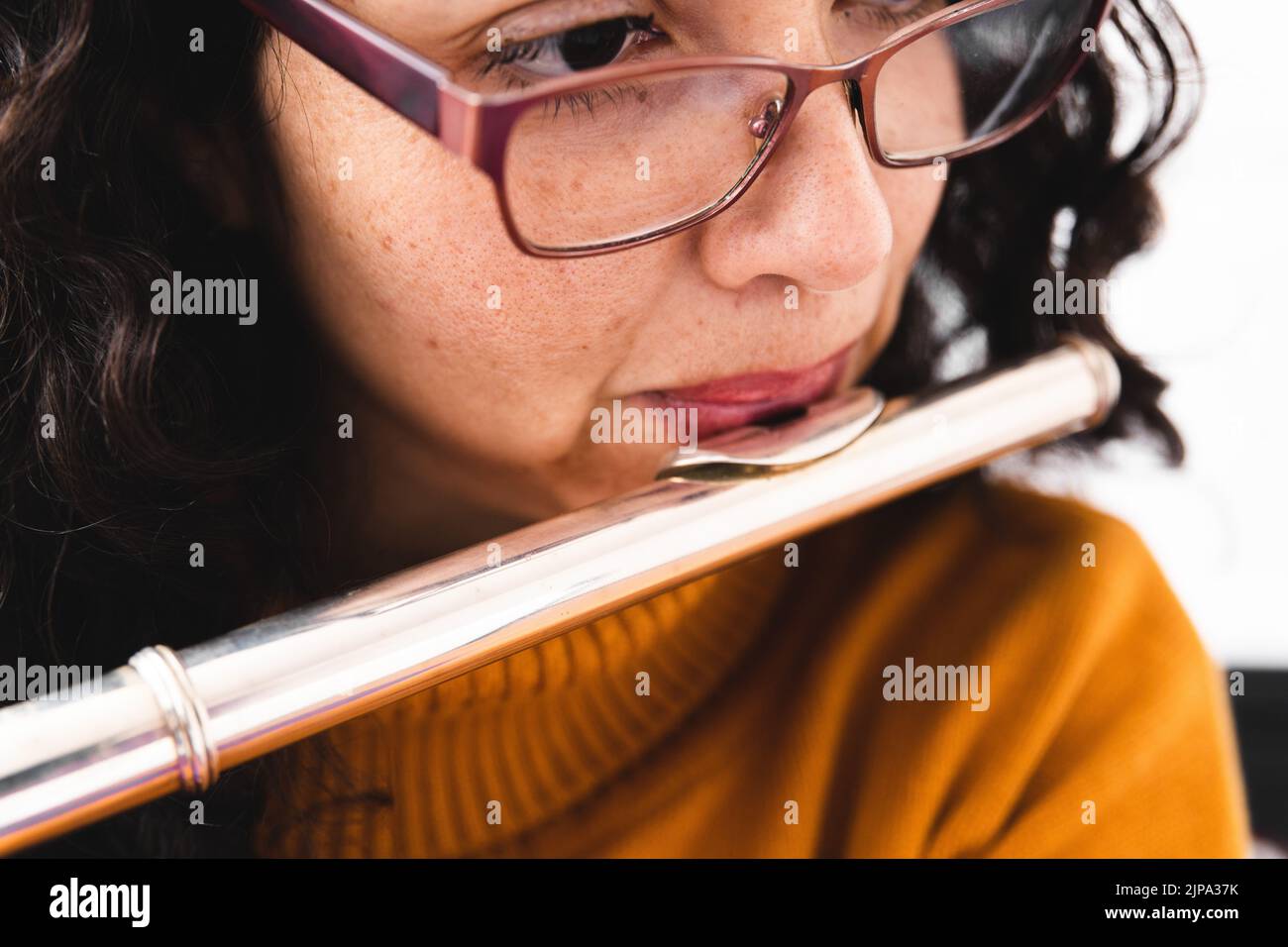 Nahaufnahme einer Brünette, die einen gelben Pullover trägt und eine Querflöte spielt Stockfoto