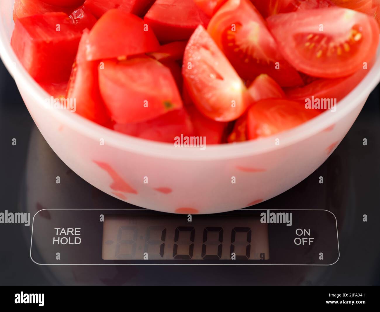 Eine Schüssel mit einem Kilogramm Tomatenscheiben auf digitaler Skala. Stockfoto