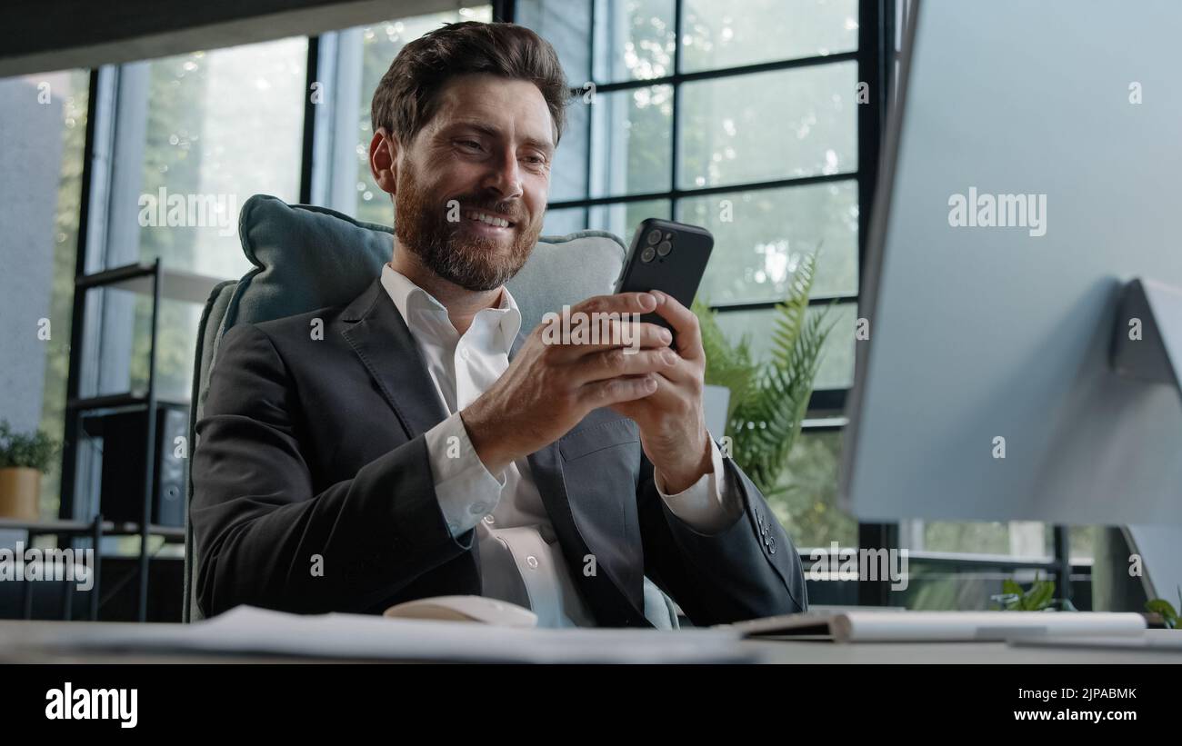Beschäftigter kaukasischer bärtiger Mann mittleren Alters 40s Geschäftsmann nutzt Handy-App SMS Chat SMS-Nachricht arbeiten im Büro Schreibtisch mit Stockfoto