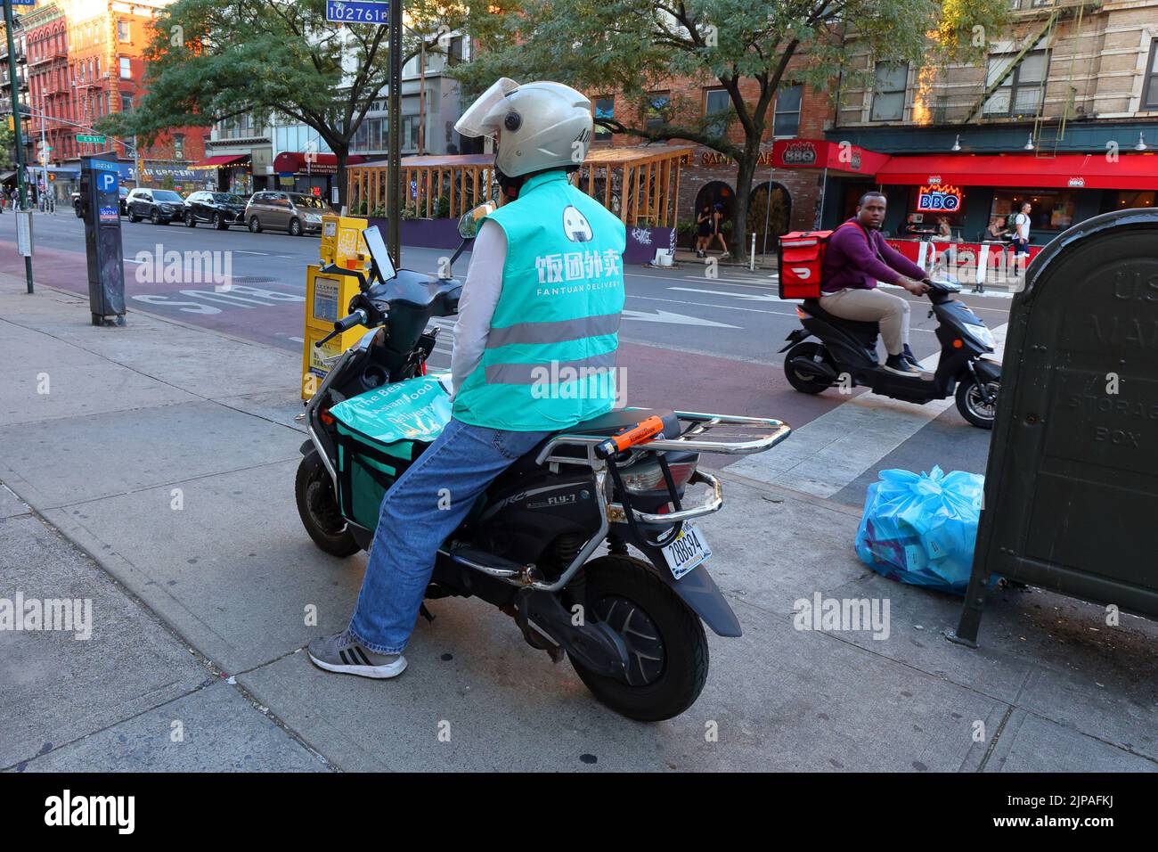 Fantuan Delivery und Grubhub Delivery Workers on Electric Mopeds in Manhattans East Village Nachbarschaft, New York City. 飯糰外賣 Food Delivery Gig Arbeiter. Stockfoto