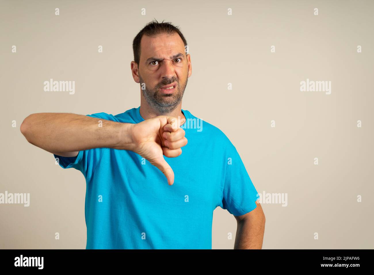 Junger, hübscher Mann mit einem lässigen blauen T-Shirt auf einem isolierten beigen Hintergrund, der unglücklich und wütend aussagt und Ablehnung zeigt und mit dem er negativ umgeht Stockfoto