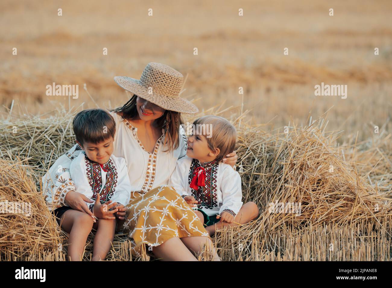 Ukrainische Jungen und Mutter sitzen nach der Ernte auf dem Weizenfeld zusammen. Familie, Freunde halten die Hände. Kinder sind unsere Zukunft. Frohe Kindheit. Stockfoto