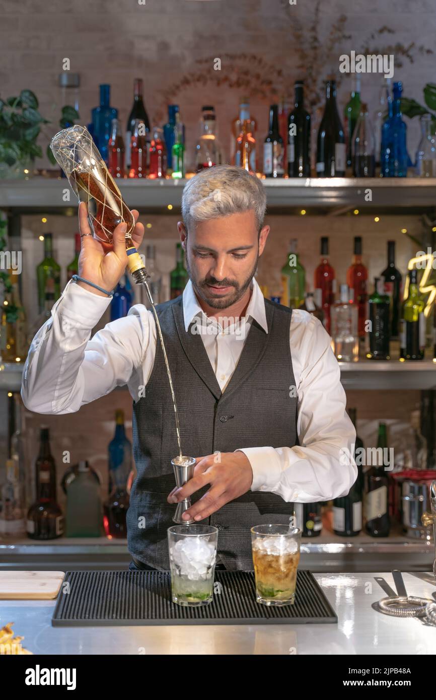 Eleganter Barkeeper, der im Nachtclub einen Cocktail aus Mojito zubereitet, Zutaten hinzufügt und an der Theke Expertengetränke kreiert. Stockfoto